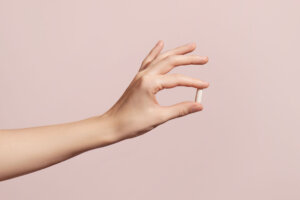 Hand holding the supplements on pink background