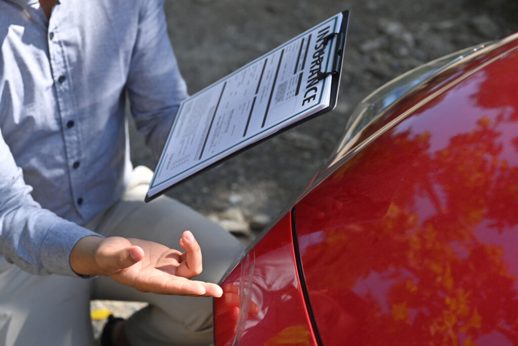 Cropped shot insurance agent holding insurance claim form and inspecting damaged car.
