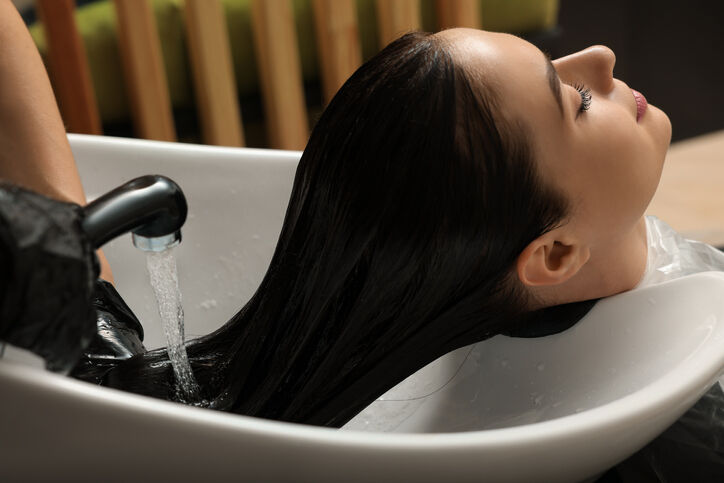 Hairdresser rinsing out dye from woman's hair in beauty salon