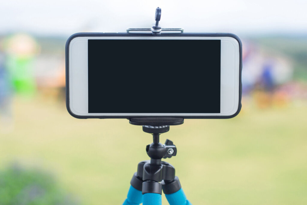 Smartphone on a tripod with tree backdrop with sky and clouds