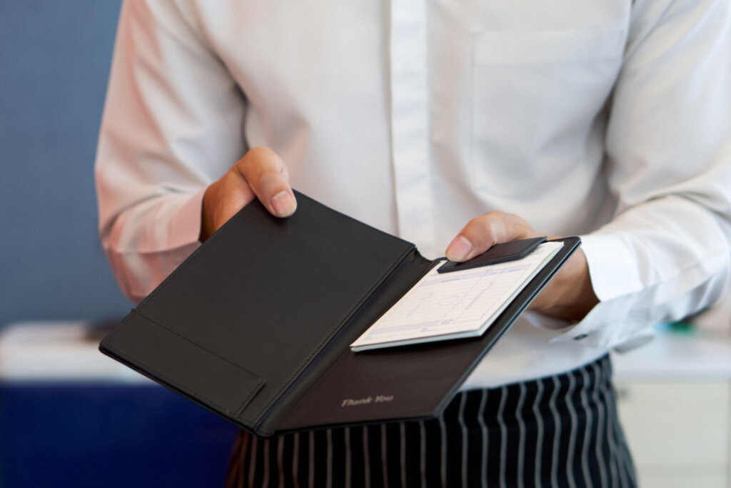 The waiter in a white shirt and apron presents a receipt after calling the bill.
