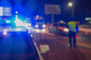 Unrecognizable blurry police car lights and police force officer on night road background, crime scene, night patrolling the city. Abstract defocused image.
