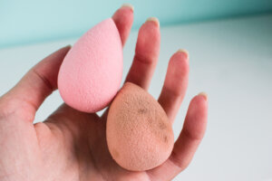 Pink beauty tear shaped blender, dirty and clean sponges isolated on white background. Cosmetic tool for makeup in hand.