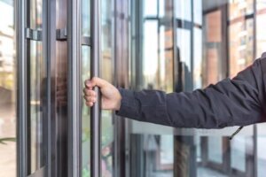 Man's hand holding the handrail is about to open the glass door of the building