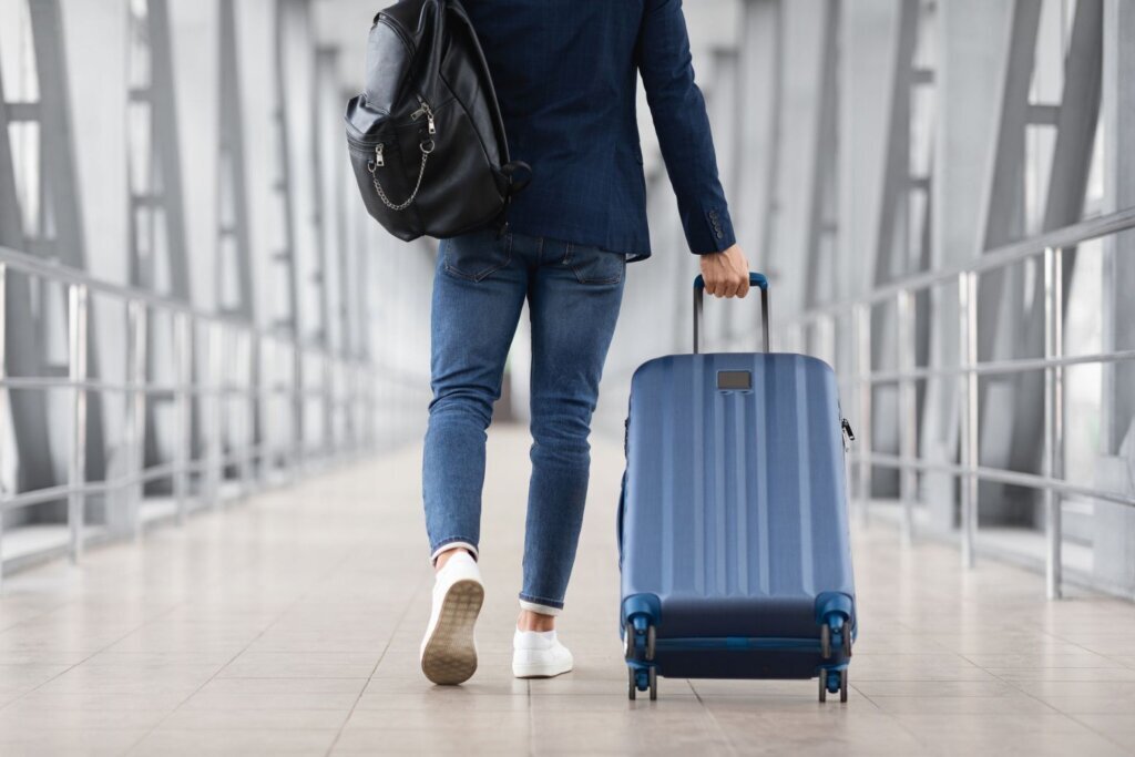 Unrecognizable Man With Bag And Suitcase Walking In Airport, Rear View
