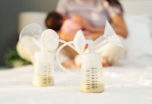 The breast milk are in the bottles of electric breast pumping set on bed with mother breastfeeding newborm baby background