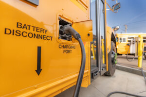 Yellow electric school bus plugged in at a charging station.