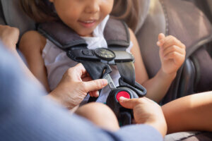 Parent buckling her child's seat belt in the car. Transportation safety.