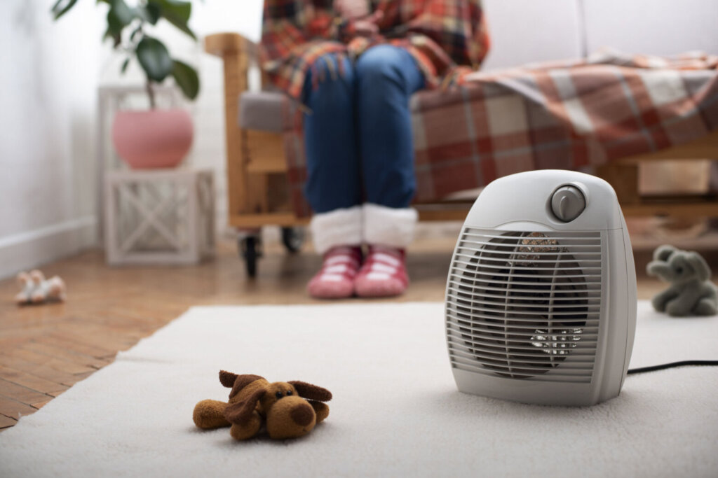 Electric fan heater on the floor in living room with human sitting on the sofa at background
