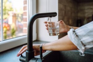Water filtration in domestic kitchen. Unrecognizable woman hands pouring water in drinking glass from tap