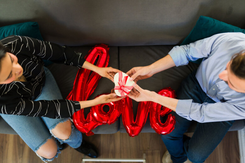 Young couple exchanging heart shaped gift on valentine's day with a red love balloon on the sofa