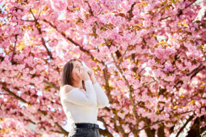 Woman allergic suffering from seasonal allergy at spring, sneezing, blowing nose with handkerchief.