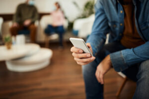 Close up of man using cell phone in waiting room at medical clinic.