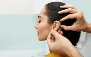 Installation hearing aid on woman's ear at hearing clinic, close up, side view. Deafness treatment, hearing solutions