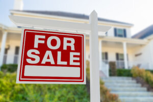 'For Sale' real estate sign in front of beautiful house