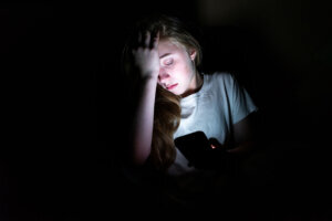 Upset girl on her smartphone in the dark.