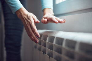 Woman heating her hands on the radiator during cold winter days.