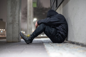 Depressed hooded man sitting on a street during night time.