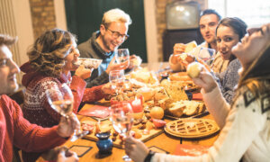 Front view of friends group tasting christmas sweets food and having fun at home drinking champagne sparkling wine Winter holidays concept with people enjoying time eating together Warm filter