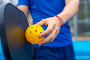 Hand holding pickleball ball and paddle on court