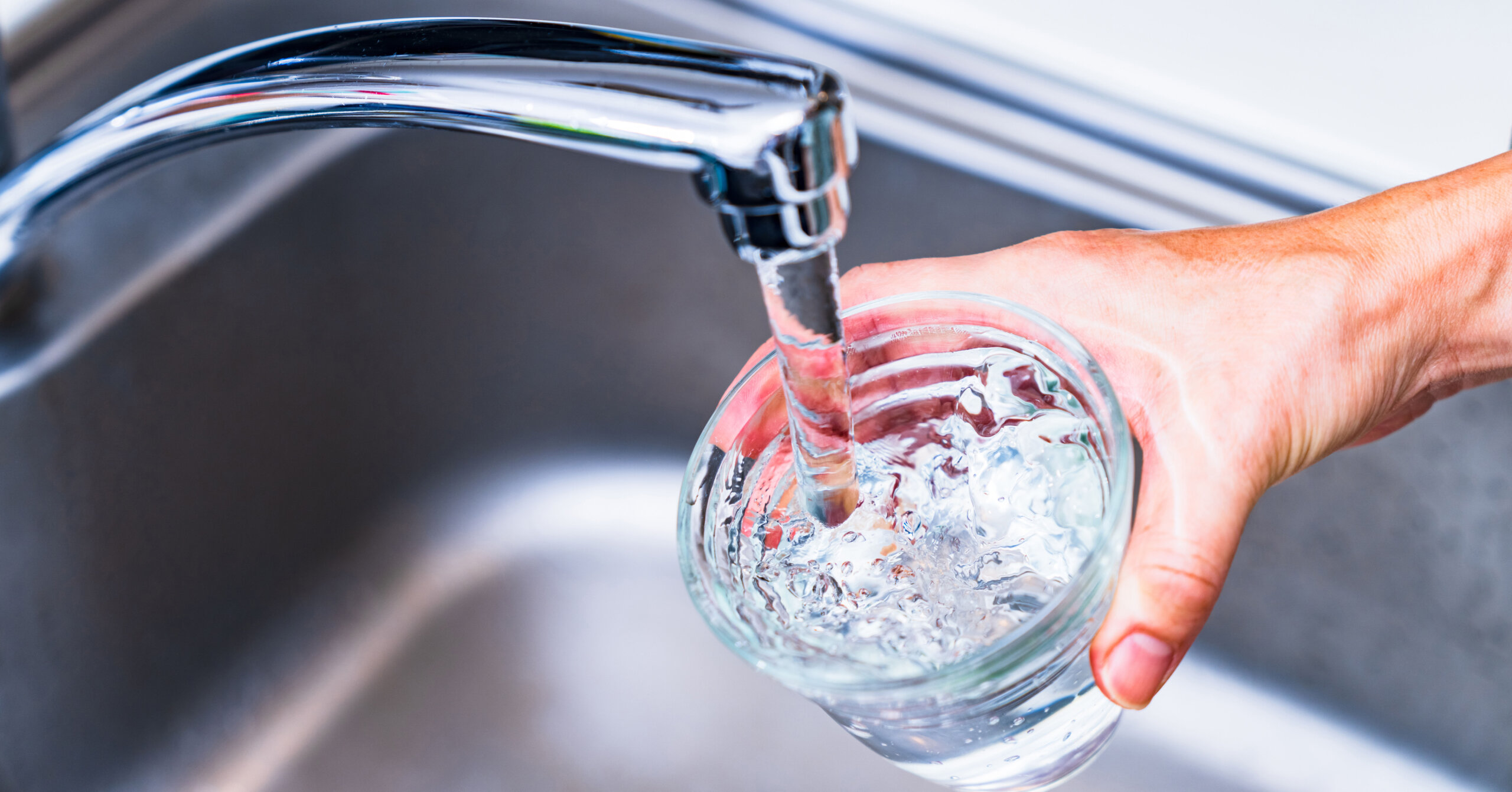 Woman hand holding cup under running sink