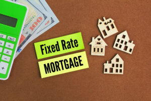Shape of a wooden house, calculator, paper money and colored paper with the word 'fixed rate mortgage'