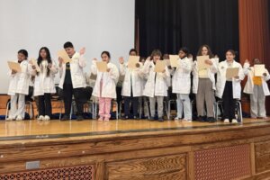 Harriet Tubman Elementary School students on stage in white doctor coats