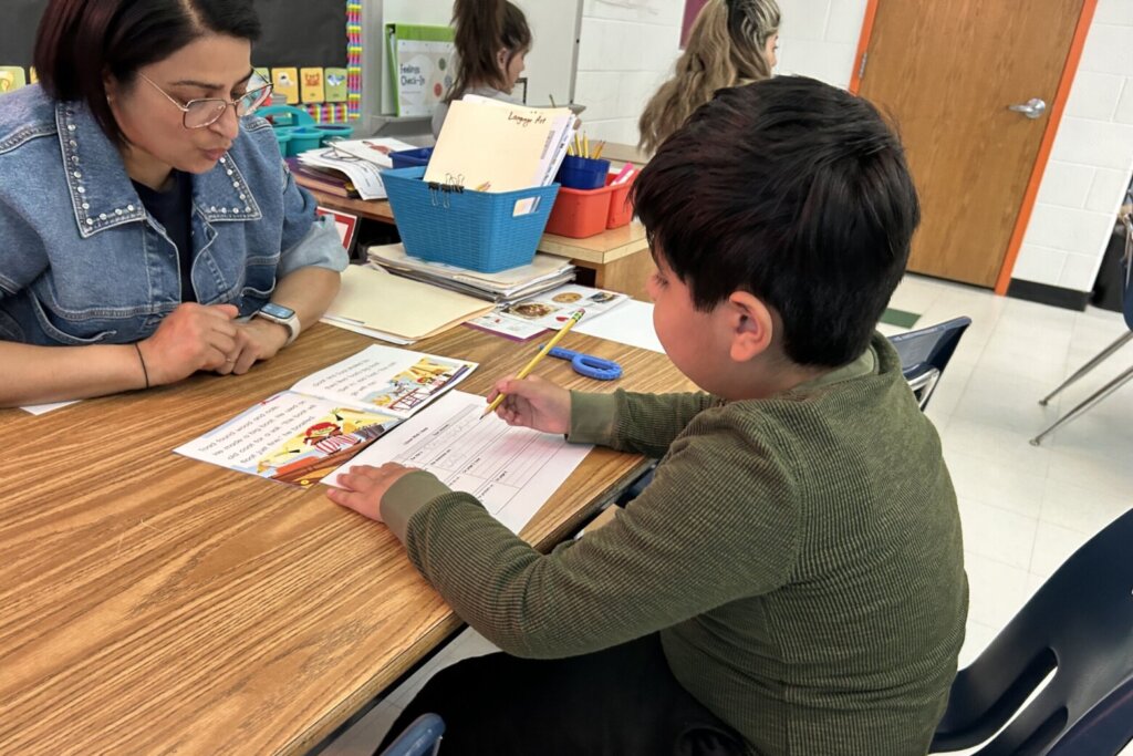 Student works at table with his teacher Nuril Kingsley across