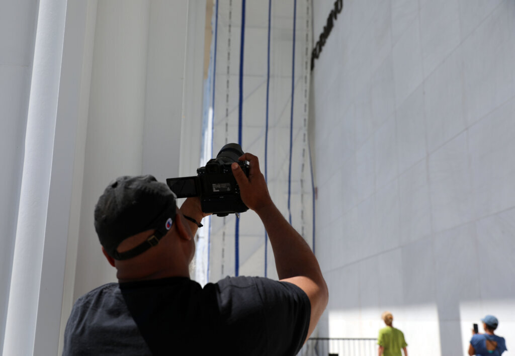 A person takes a photograph of the tarp over the sign at The John F. Kennedy Center for the Performing Arts, in Washington, Saturday, June 13, 2026. (AP Photo/Rahmat Gul)