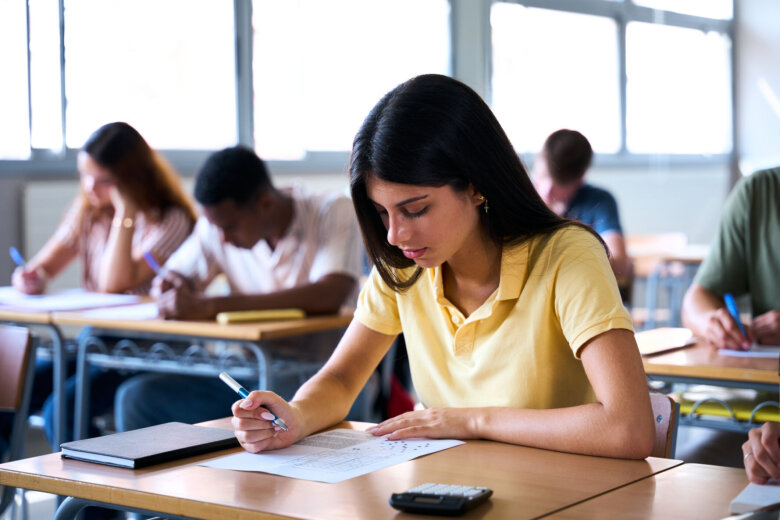 Focused student taking exam in classroom with calculator and notebook