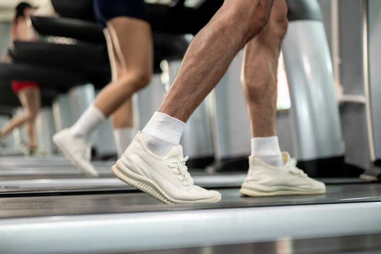 Close up of man and woman client's legs with sneaker shoes exercising by running on treadmill in gym