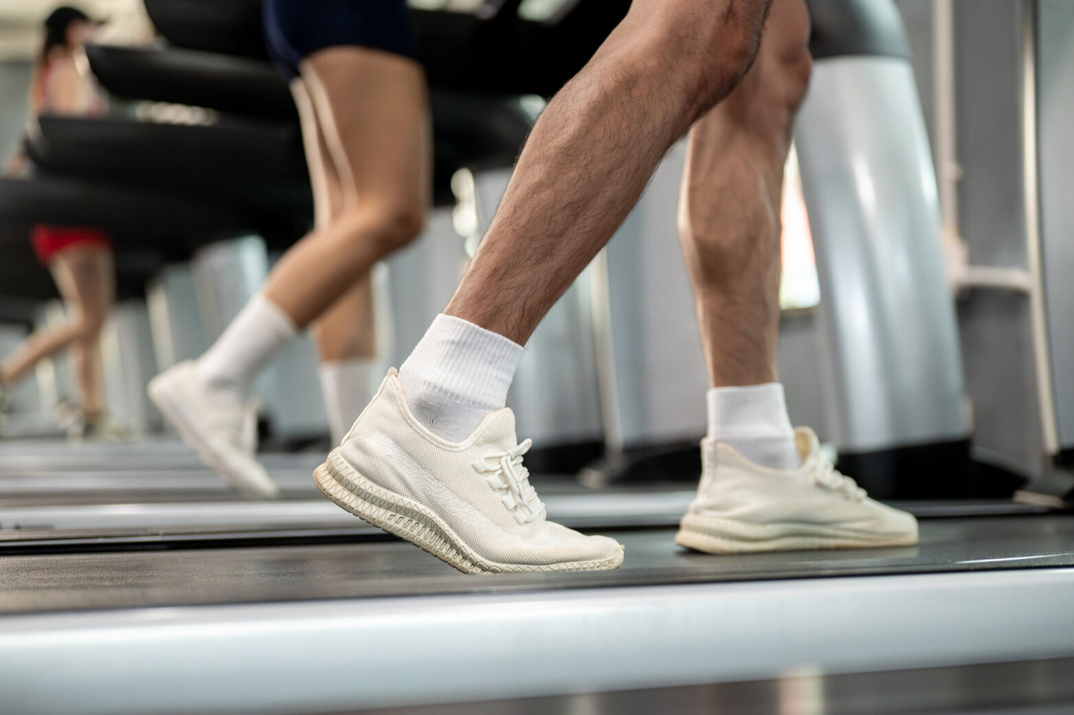 Close up of man and woman client's legs with sneaker shoes exercising by running on treadmill in gym