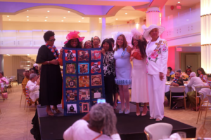 Group of weman stand for photo holding quilt