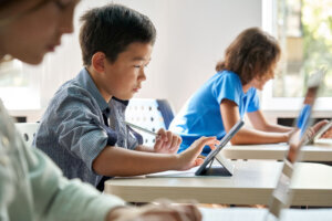 Focused Asian school boy using digital tablet at class in classroom.