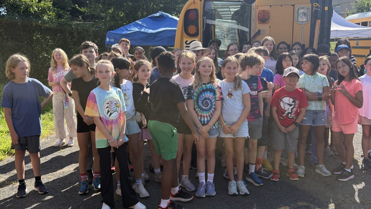 Group of students pose for photo in front of overturned school bus